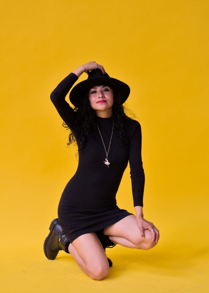 woman in black dress and hat kneeling in studio